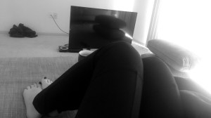 a black and white photo of my legs curled up on the base of the couch, my tv on the floor in the distance having freshly moved into this apartment