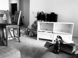 A black and white photo of inside my apartment with pieces of furniture strewn about surrounded by boxes and packing paper