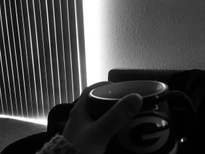 A black and white photo laying on the couch viewing the shuddered shades, my arm extended holding a coffee mug