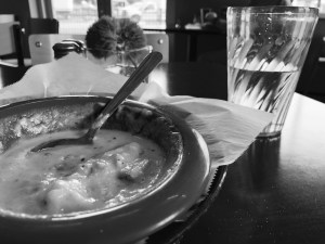A black and white photo of a partially eaten bowl of soup and glass half full of water