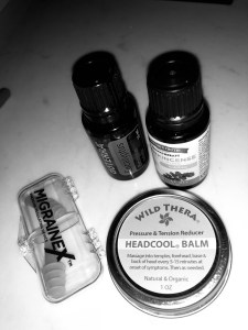 A black and white photo of some migraine "cures" including some essential oils, wild thera's headcool balm, and migraineX ear plugs