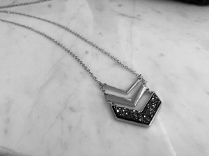 a black and white photo of a v shaped three tiered necklace against a marble backdrop