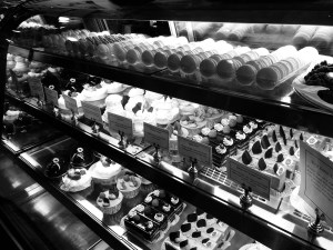 a black and white photo of a dessert counter full of rows of macarons and fancy cupcakes and pastries