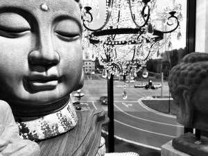 a black and white photo of a ceramic buddha head surrounded by chandeliers overlooking an intersection outside the window