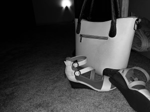 a dark shot in black and white, camera flash illuminating my white purse and white sandals tossed at it's base