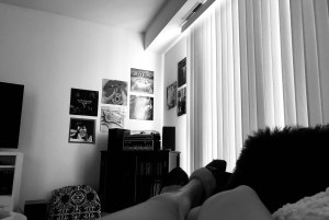 a black and white photo of my legs sprawled out on my couch in my current drawn living room, record albums hung on the wall in the distance