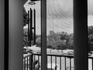 a black and white photo through my screen door looking at my windchimes on a stormy day