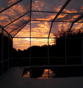 a vibrant sunset through the covered netted in pool patio 
