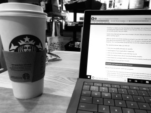 a black and white photo of my laptop open at a coffeeshop with my starbucks coffee on the left 