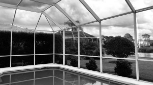 a black and white photo of a screened in and covered pool porch with clouds in the distance 