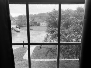 a black and white framed view out my window overlooking the rain pouring down flooding the culdesac