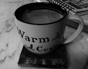 a black and white photo of a white mug that says warm and cozy, full of chai 