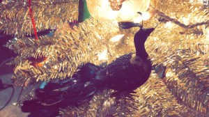 a close up of a tinsel christmas tree with a peacock ornament in center view