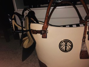 a dimly lit photo of a pair of black stilettos dangling off my large creamy purse