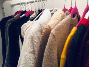 a view of thick sweaters arranged by color hanging in my closet 
