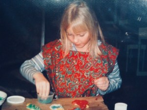 a photo of me as a child, i'm wearing a blue striped shirt with a red apron over it decorating christmas cookies