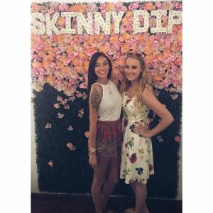 a photo of me and my best friend, two white girls she's a brunette on the left I'm blonde on the right standing in front of a floral display with pink flowers fading to green grass that says "skinny dip"