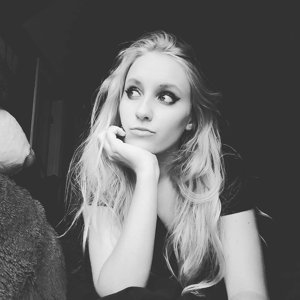 Black and white photo of white woman with long blonde hair. Her head is resting on her hand and she's looking longingly into the distance away from the camera.