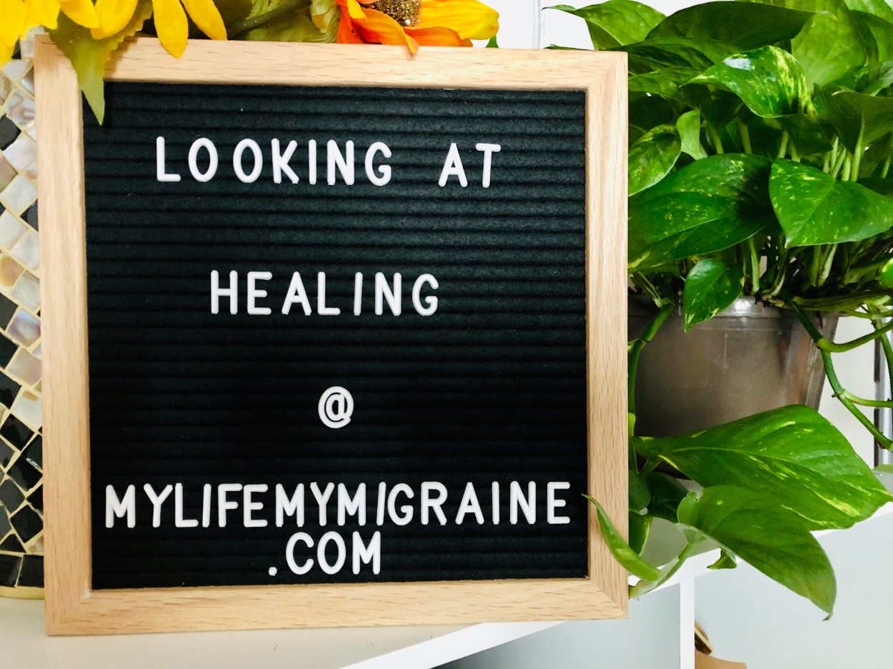 Black felt board with text "looking at healing" with a large green pothos plant behind it.