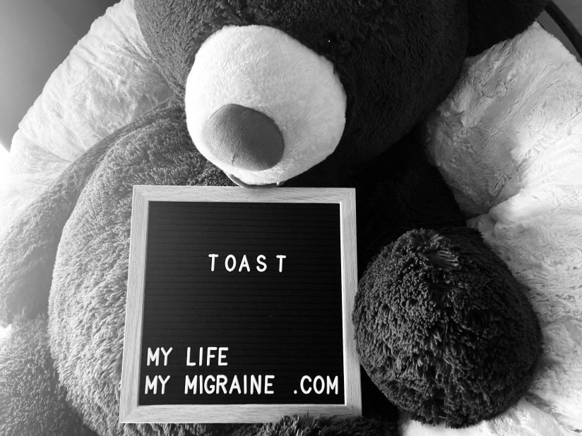 Black and white image depicting a large teddy bear holding a felt board sign that says "toast"