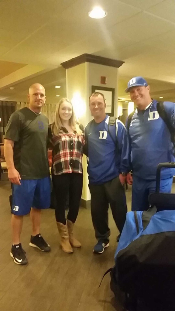 Girl in flannel and cowboy boots posing for photo with three staff members on the Duke Baseball team. 