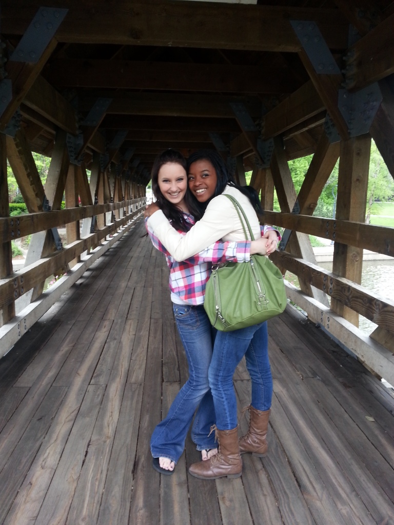 Two girls hugging each other on a bridge laughing. 