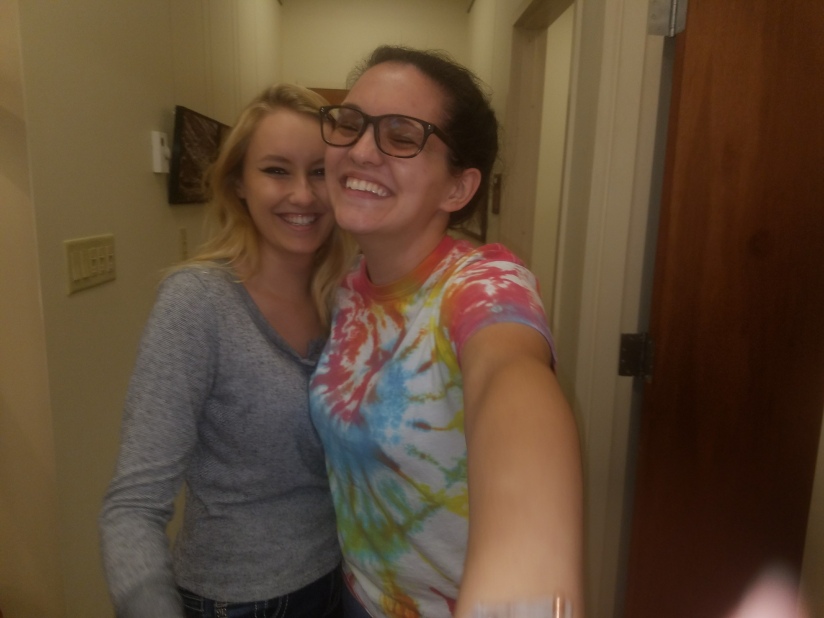Two girls posing and laughing in a hallway. One is in a grey shirt, the other a tye-dye t-shirt. 