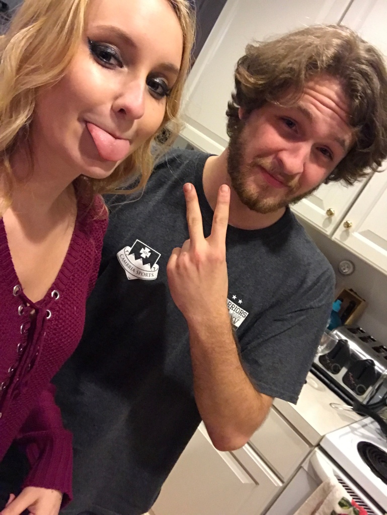 Blonde girl sticking out her tongue, brunette guy with shaggy haircut throwing up a peace sign.