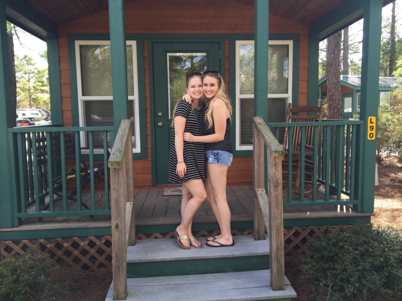 Two girls posing in front of a log cabin rental. 