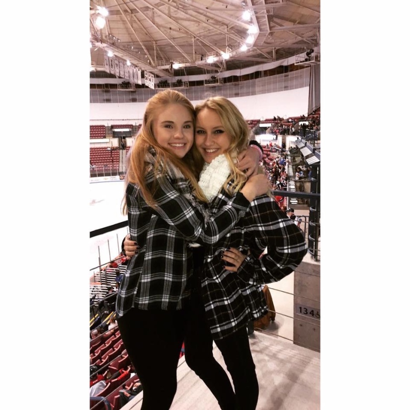 Two girls in matching flannels hugging at a hockey game. 
