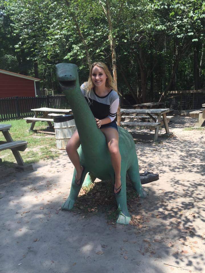 Blonde girl sitting on top of a long neck dinosaur. 
