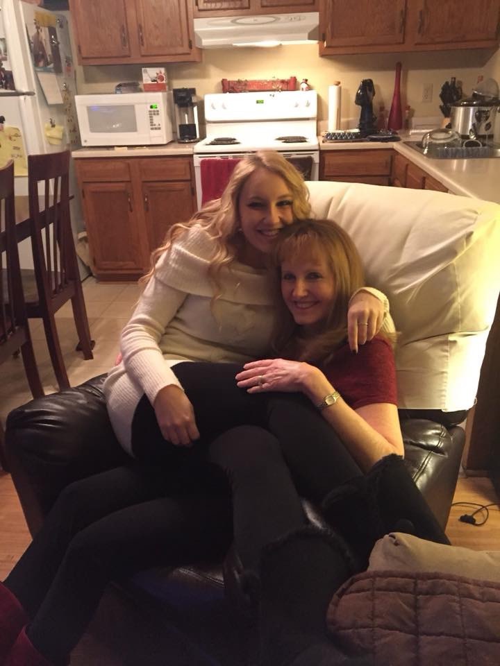 Photo of blonde girl sitting on top of her mother, squishing her before a holiday party. 