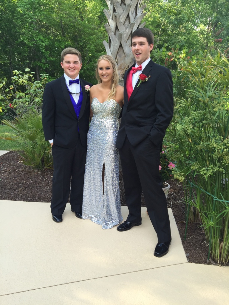 Girl in silver prom dress posing with two gentlemen in tuxes. 