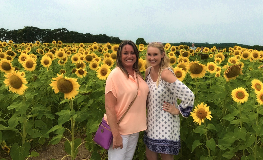 Two sisters standing in front of a very large sunflower field. 