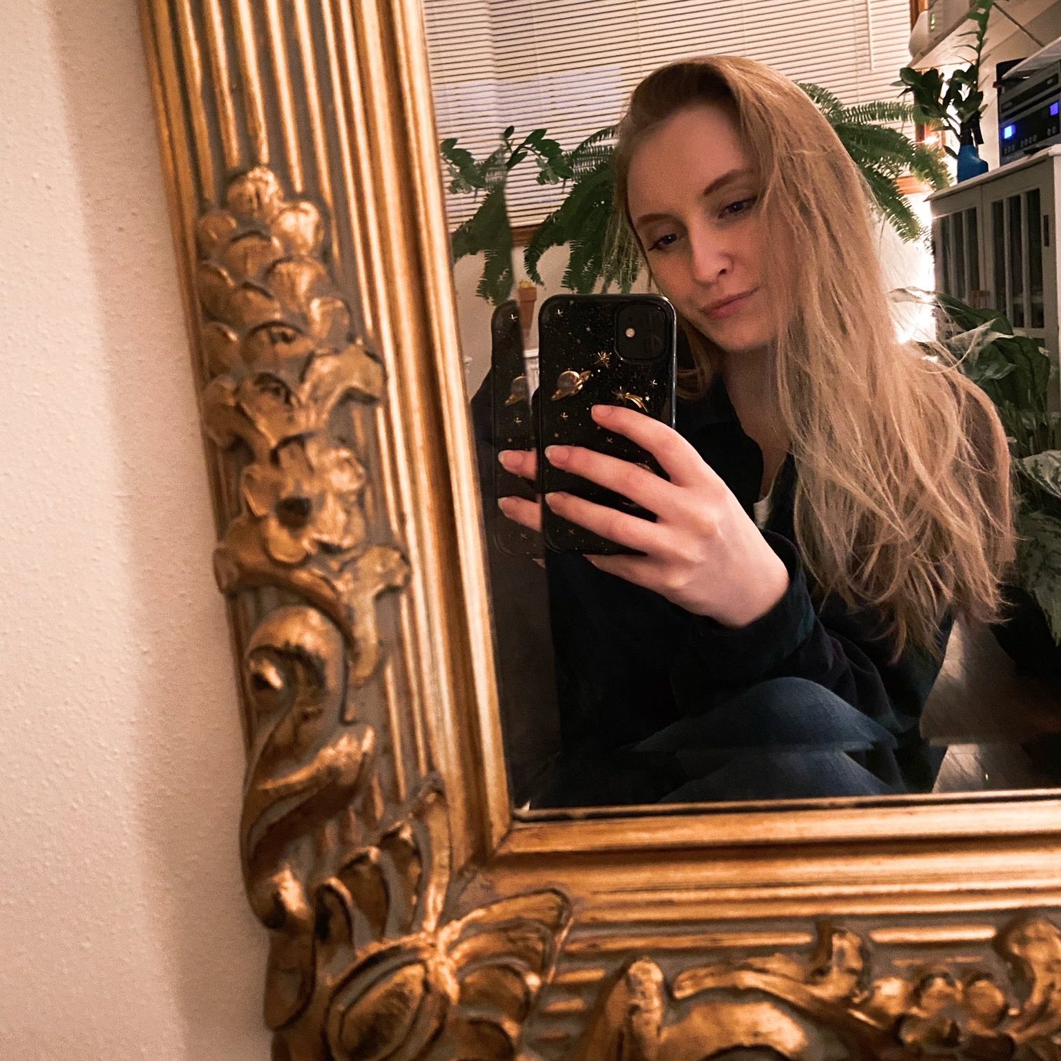 Blonde white woman taking a selfie in a large gold framed mirror.