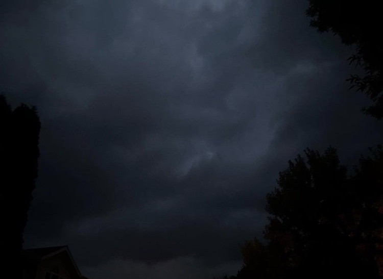 Dark nighttime sky, tree silhouettes bordering the frame with ominous dark storm clouds rolling in