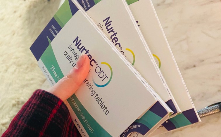 Hand holding three packets of Nurtec prescriptions