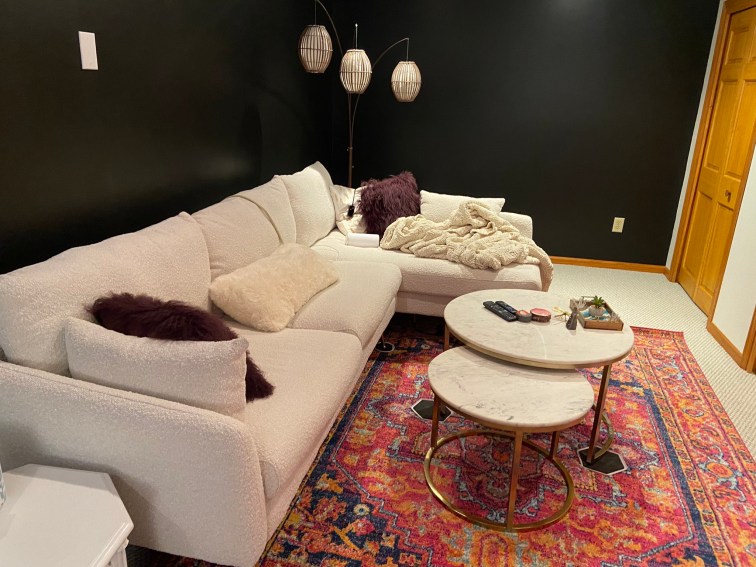 The white boucle sectional has been placed back on the left wall against the new black paint. It sits atop a brand new pink oriental patterned rug with two marble nesting tables atop it. My old small tiki three pendant floor lamp sits in the corner.