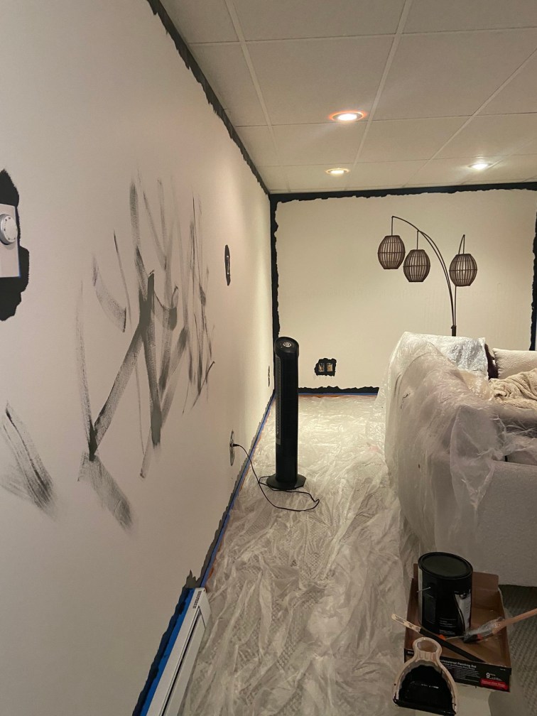 View into my living room as painting progress has started, the edges of the once white walls are now done in black. The center of the longest wall has abstract black brush strokes across it where I got excess paint off my brush.