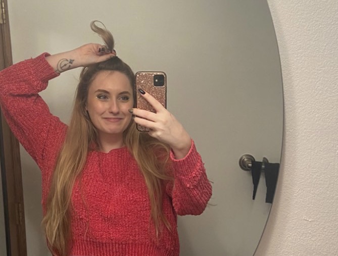 Me taking a selfie in the mirror. I'm in a pink sweater, my long blonde hair cascading down to my waist. I'm holding up a small chunk of hair maybe 4 inches long like cindy lou hoo. 
