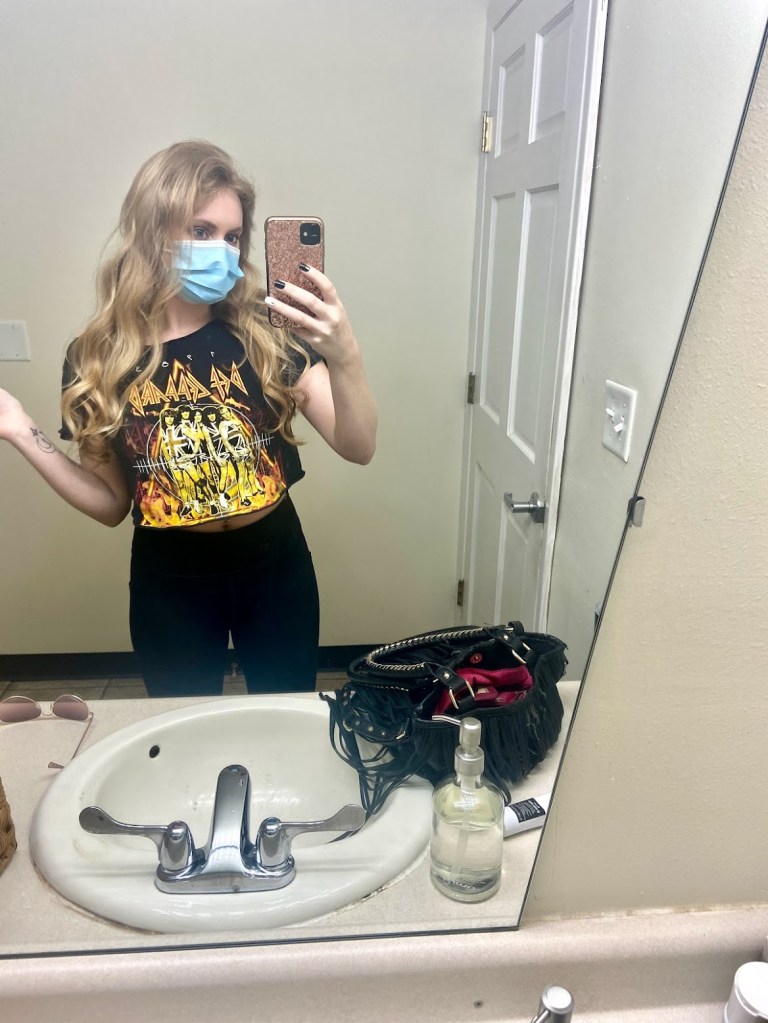 A selfie at the hair salon in the bathroom, my hair is curled and an even blonde tone. I'm wearing a blue face mask. 